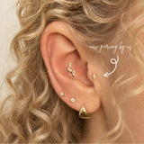 DOVIANA 14K solid gold oval CZ threadless labret flat back earring styled in a curated ear stack on a model with curly blonde hair.