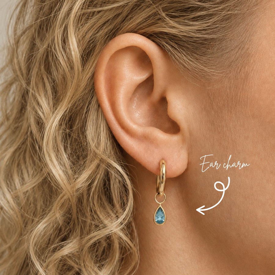 DOVIANA 14K solid gold teardrop blue topaz ear charm worn on a gold hoop by a model with curly blonde hair.