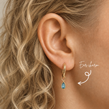 DOVIANA 14K solid gold teardrop blue topaz ear charm worn on a gold hoop by a model with curly blonde hair.