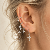 DOVIANA four-petal CZ flower ear charm made from silver-tone titanium, shown on a hoop in a curated ear stack. Charm sold individually; hoop not included.