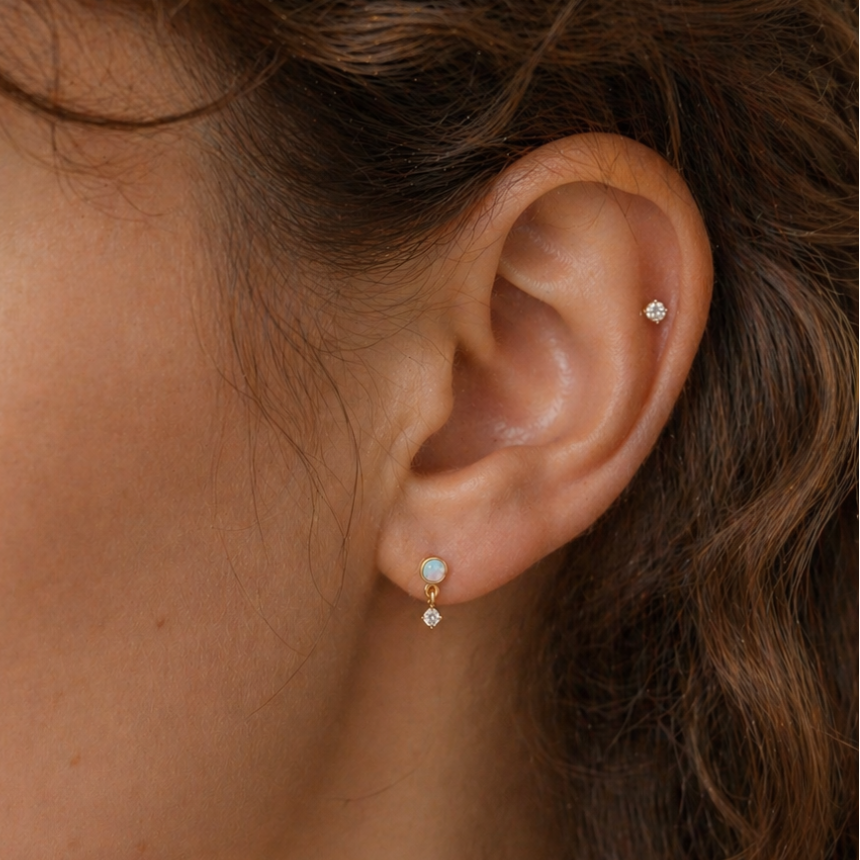 14K gold opal dangle flat back earring on a real human ear with soft curly hair, featuring a small diamond stud helix piercing, natural skin texture and minimal luxury jewelry styling by DOVIANA NYC