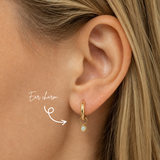 Blonde woman wearing a DOVIANA 14K solid gold round opal ear charm in a polished bezel setting on a hoop, highlighted by an arrow.