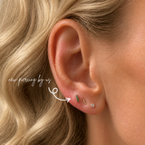 Close-up of a white woman with curly blonde hair wearing a DOVIANA 14K solid gold bar triple green CZ threadless labret flat back earring on the lobe, styled with a minimalist gold bar stud and diamond stud, natural skin texture and soft lighting.