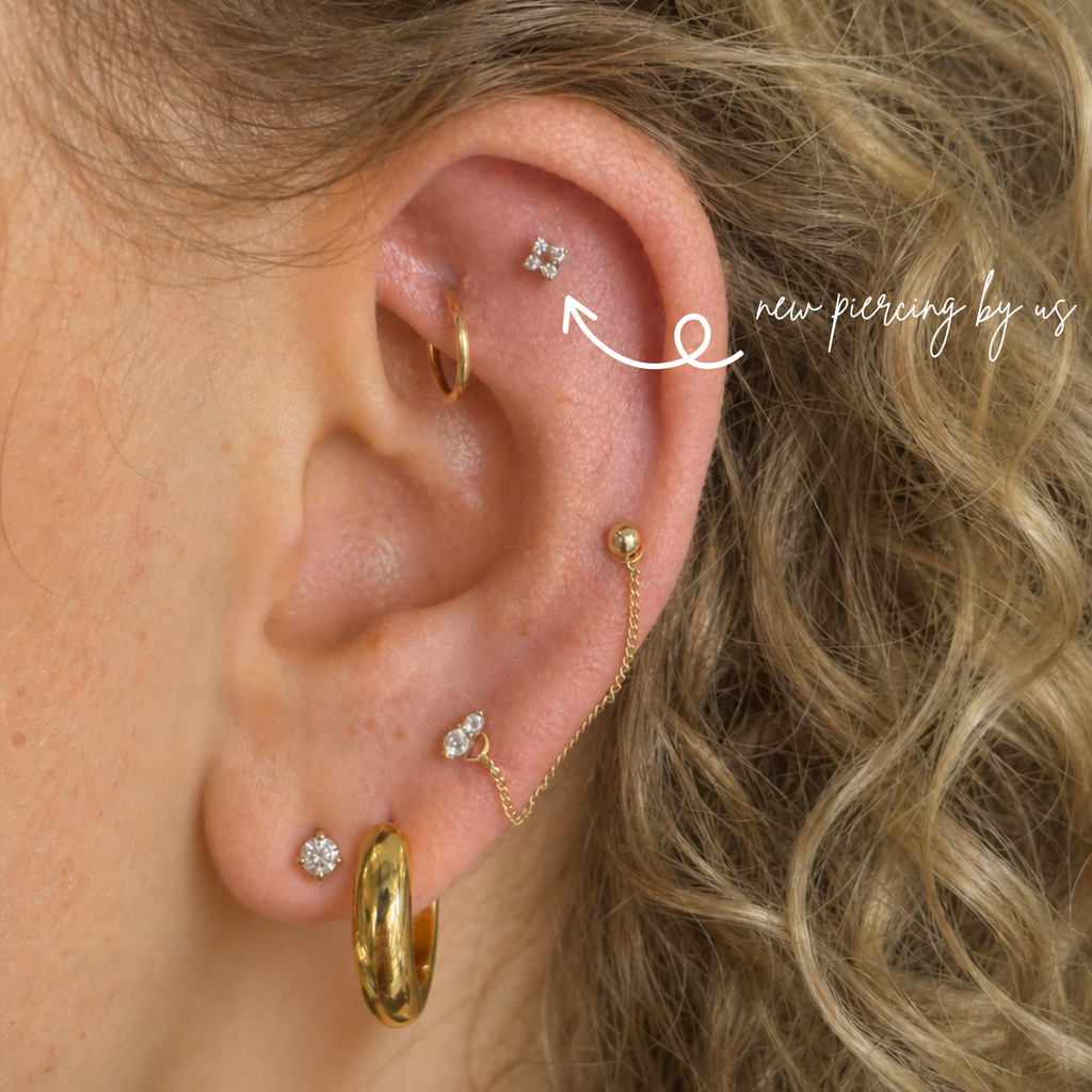 Close-up of a white woman with curly blonde hair wearing a 14K solid gold four-point cluster CZ threadless flat back earring on the helix, paired with a diamond stud on the lobe, showcasing natural skin texture and a curated ear stack in soft lighting