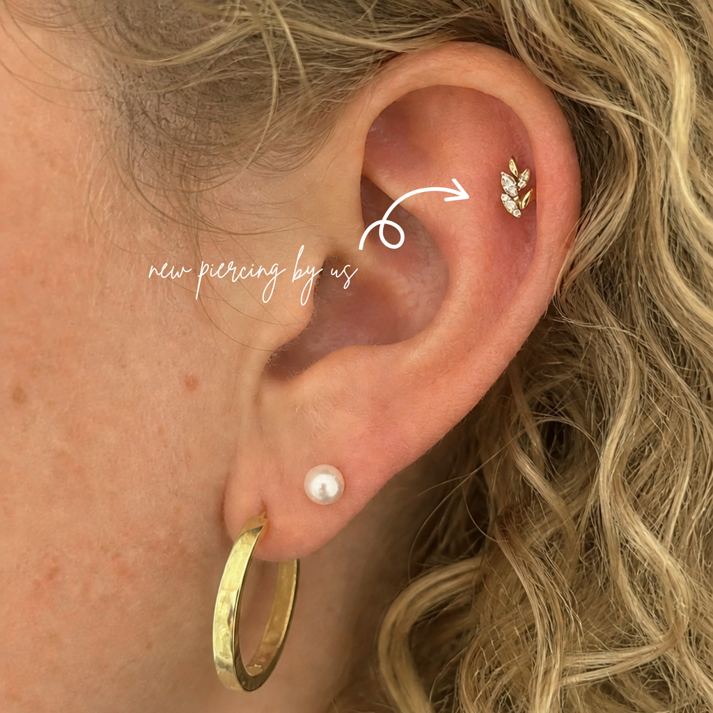 Close-up of a white woman with curly blonde hair wearing a DOVIANA 14K solid gold marquise CZ leaves olive branch threadless flat back earring on the lobe and a small diamond stud on the helix, natural skin texture visible