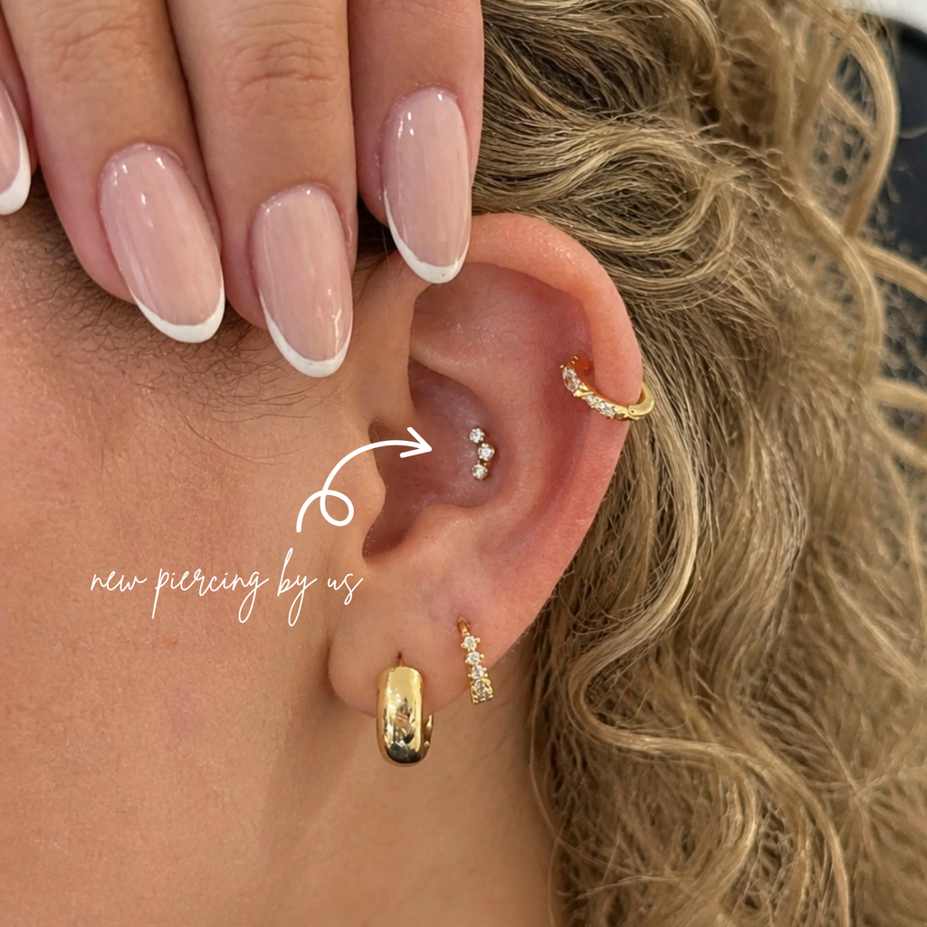White woman with curly blonde hair wearing DOVIANA 14K solid gold triple CZ barnacle trio curved bar threadless labret flat back earring on lobe, featuring three dainty cubic zirconia stones in a curved design with natural skin texture visible