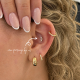 White woman with curly blonde hair wearing DOVIANA 14K solid gold triple CZ barnacle trio curved bar threadless labret flat back earring on lobe, featuring three dainty cubic zirconia stones in a curved design with natural skin texture visible