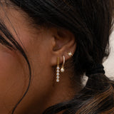 Sterling silver earrings with thick 18K gold plating styled on ear, featuring CZ drop dangle, huggie hoop, and stud for a curated ear stack, elegant everyday jewelry by DOVIANA NYC.