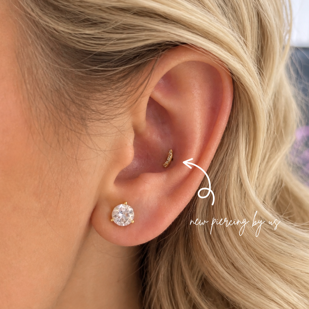 Close-up of a blonde woman’s ear featuring a DOVIANA conch piercing with a 14k solid gold curved CZ flat back earring and a diamond stud on the lobe, showcasing professional ear piercing and curated ear styling in NYC.