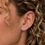 Close-up of a woman with curly blonde hair wearing DOVIANA graduated double marquise CZ threadless labret titanium flat back earring on the lobe and a small CZ stud on the helix, featuring a minimal and elegant everyday piercing style.
