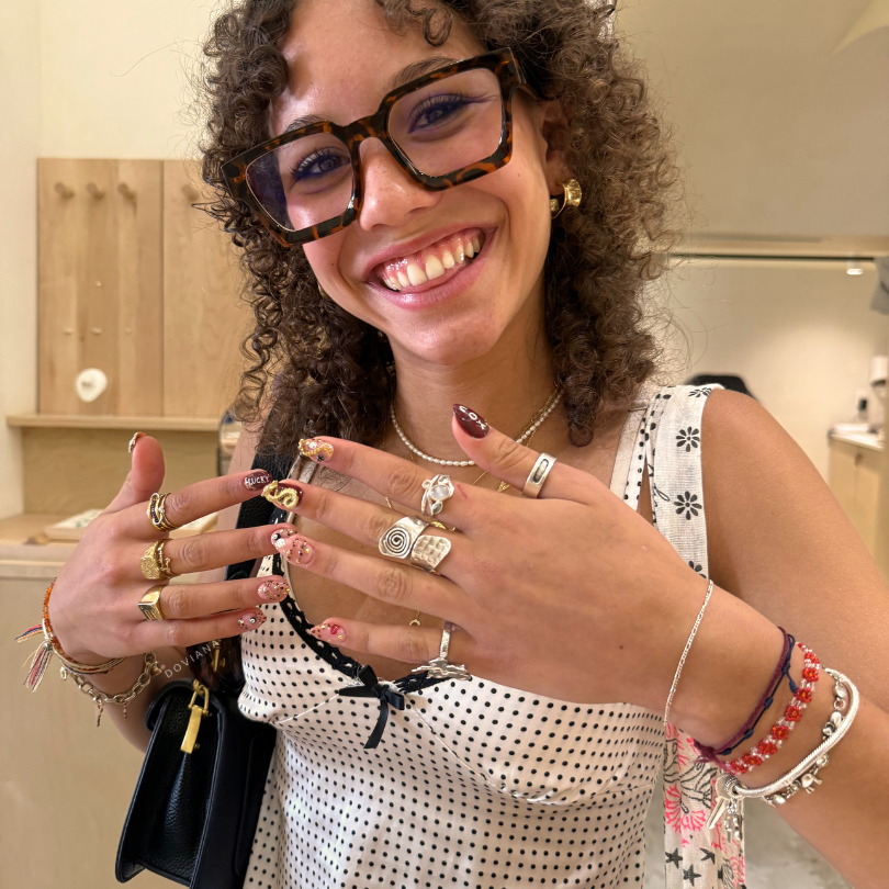 Smiling customer showing stacked DOVIANA permanent bracelets and charm bracelets in New York City featuring gold-filled jewelry and layered everyday wrist styling.