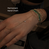 Close-up of a gold permanent hand chain bracelet connected from finger to wrist, layered with multiple gold and green beaded bracelets, showcasing dainty luxury jewelry and permanent hand chain styling in NYC.
