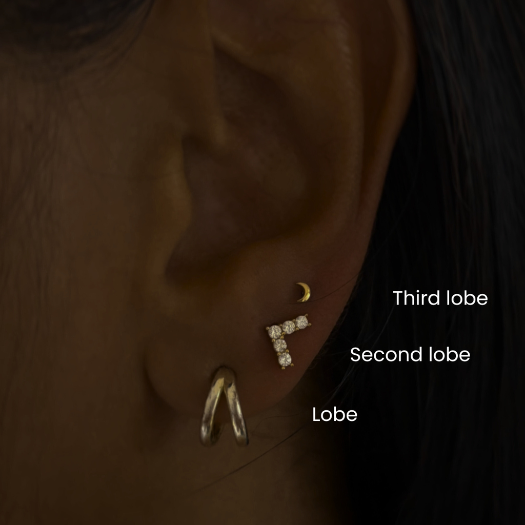 Close-up of ear with DOVIANA third lobe, second lobe, and lobe piercings featuring gold and diamond earrings, showcasing curated ear stacking and professional ear piercing placement in NYC.