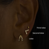 Close-up of ear with DOVIANA third lobe, second lobe, and lobe piercings featuring gold and diamond earrings, showcasing curated ear stacking and professional ear piercing placement in NYC.