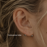 Close-up transverse lobe ear piercing by DOVIANA featuring implant-grade titanium barbell jewelry and professional needle piercing service in NYC with minimalist curated ear styling.