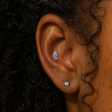 Close-up of ear wearing an evil eye Hamsa hand threadless flat back earring in silver titanium, styled with a diamond stud on the lobe, shown on a Black woman with natural curly hair at DOVIANA NYC